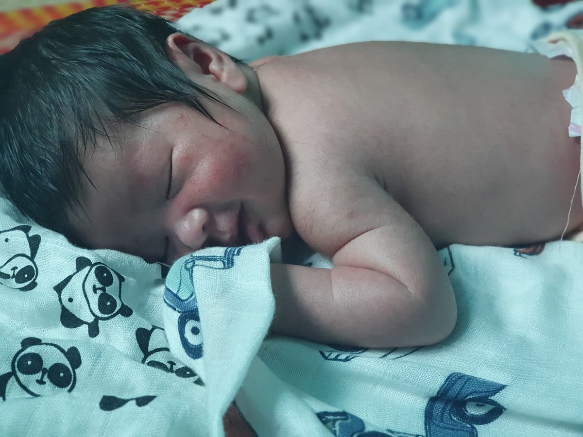 Mẹ nhớ dự sanh là 12 nhưng mãi đến khuya 13 mẹ mới có những cơn đau khó chịu. Đến sáng 14 thì nhiều hơn và mẹ hầu như không thể nằm. Mẹ linh cảm ngày mong chờ con ra đời đã tới. Mẹ bắt đầu note lại cơn gò và sẵn sàng tâm lí vào viện. 
14h hơn, mẹ - ngoại và ba lên đường đón con. Lúc này mẹ còn tỉnh lắm, trên xe hết chỉ đông chỉ tây rồi tám chuyện đủ thứ, chỉ ngoại là lo lắng ra mặt.
Dịch nên ngoại đành ở ngoài, cho mẹ và ba vào làm thủ tục. Mẹ vào khám, bs bảo 3p rồi, ra làm giấy tờ nhập viện. Quào, sắp gặp con yêu, bủn rủn rồi nhưng hớn hở lắm. Mẹ tung tăng ra ngoắc ngoắc ba đi đóng viện phí. Bụng đau râm rang nhưng không hé miệng rên rỉ tiếng nào.
Mẹ được vào phòng chờ, đo tim thai và cơn gò. Lúc này mẹ vẫn đủng đỉnh lắm, nhìn bốn bề xung quanh ai cũng lăn lộn, riêng mẹ chỉ cảm thấy đói thôi. Tự nhiên thèm ăn nui kinh khủng. 
Chờ mãi cũng được tiếp tế đồ ăn, mẹ hí hửng ăn 1 lèo hết tô rồi lên giường nằm tiếp. Ngủ thiếp đi một lúc, khi tỉnh thì 22h rồi. Lại đói. May ghê, chắc ngoại hiểu cái nết láo ăn của mẹ nên có đăng kí tiếp tế lương thực hiệp 2, thế là mẹ được phát 2 hộp sữa. Mẹ ngồi đung đưa dò uống 1 lèo trong khi cô kế bên cứ la oai oải: 
- Đau quá 😱 đau chết mất, bác sĩ ơi...
Cổ đạp cả vào thành giường của mẹ. Mẹ hơi quạu vì vẫn còn say ke và thật sự cần nằm nghỉ. Bụng bảo dạ, chịu tí chứ gì mà la dữ z 🙄🙄🙄 ấy vậy mà chưa tới 5p sau khi tự thân đi vứt hộp sữa, mẹ cảm nhận cơn gò bắt đầu lên level, mẹ bắt đầu ngồi k vững. Mẹ nằm và cảm nhận cơn đau đang tăng, vượt ngưỡng chịu. 15p sau, mẹ nhờ bs khám lại xem được bao nhiêu phân rồi. Chắc từ chiều do mẹ ngoan chẳng la làng nên cô nhiệt tình lại khám lẹ lắm, chứ nhiều mẹ khác la quá mà chẳng ai ngó ngàng. Vẫn chỉ 3p, cô vỗ vào đùi mẹ bôm bốp bảo - con to bằng bắp đùi á, chưa đẻ được đâu. Mẹ vui, nhưng bắt đầu thấy sợ.
1 tiếng sau, mẹ là người la to nhất phòng 🤣🤣🤣🤣 Quằn quại thật sự. Dù không muốn nhưng cơn gò tới là chẳng nhớ cần thở hay không, chỉ muốn thét lên để có ai đó trợ giúp. Và không ai cả, chỉ những câu càm ràm - đau mới đẻ dc, mới 3p sao mà đẻ, con to lắm. 
Mẹ nằm, rồi bò, rồi ngồi đủ kiểu, mẹ vốn nghĩ mình can đảm lắm, nhưng cứ 5p cơn đau ập tới, mẹ như mất kiểm soát, thèm 1 cái vuốt lưng của ba, mẹ bắt đầu tủi, nhưng k thể khóc, hay chính xác hơn chẳng còn sức để khóc.
- Bs, tiêm k đau, lẹ lên, em chết luôn chứ chịu k nổi.
Rồi với sự quằn quại của mẹ, mẹ cũng được đẩy đi tiêm
Nhưng đã tiêm liền đâu. Phải đợi. Mà đợi là 5p mẹ lại đập tay vào tường, cảm giác muốn chết đi cho xong. Chị kế bên còn suýt lọt khỏi giường. Mẹ xoa bụng năn nỉ con hợp tác vì mẹ đuối quá rồi. Mẹ bắt đầu thấy xung quanh ai chửi ai nói gì cũng tăng thêm kích động và mẹ sẵn sàng dùng chút sức tàn để phản ứng lại chứ chả năn nỉ nể nang gì nữa. Rồi mẹ cũng được tiêm con ạ. Nhưng thuốc cần tgian để thấm và mẹ vẫn đau như ai xắn ruột gan từng khúc trong bụng. Mẹ được đẩy lại về phòng chờ để tiếp tục đo gò và truyền giục sinh. Mẹ tự nói sắp gặp con rồi, cố lên 💪💪💪Và lại ngoan nằm chờ. Chân mẹ bắt đầu tê và những cú thọt tay khám trong của hộ lý không còn làm mẹ đau nữa. Nhưng cơn gò vẫn k tha cho mẹ, có điều giảm 80% đau con ạ, quyết định sáng suốt nhất dù bao người hù này nọ mẹ vẫn kiên quyết tiêm. Rồi đâu đó 1 tiếng hơn, cơn đau dồn dập hơn, mẹ được hỗ trợ chọc ối, ối vỡ, mẹ đau nhiều, nằm chút là la trong vô thức vì lại đau, thế là đc đẩy đi.
Mẹ đăng kí sanh có người thân, cứ nghĩ là ba con vô cơ, ai dè bà ngoại. Không phải ba con sợ đâu mà vì phải đổi ca cho ngoại vào. Ba bảo sợ ngoại ở ngoài đường không chỗ ngồi nghỉ. Mà thôi ai cũng dc. Miễn là mẹ đừng 1 mình. Vì... mẹ sợ mẹ chết không ai bên cạnh. Người ta vẫn bảo cửa sanh là cửa tử còn gì.
Mẹ bắt đầu đau mất kiểm soát. Quên cả thở dù ở nhà xem youtube đã tập kĩ là thở làm sao. Mẹ bị quát rất nhiều, ngoại phải cho tiền ngta mới dịu dàng ân cần lại với mẹ. Khúc này mới thấy bà ngoại vào là 1 sự may mắn với mẹ. Vì nếu là ba con thì 1 là ba gây lộn với người ta và mẹ sẽ bị rạch tan nát 🦋, 2 là mẹ bị chửi te đầu vì ba đâu biết mấy vụ "🤫💸🤭" này đâu 😂
Được 1 lúc thì mẹ ói. Ói lênh láng sạch sẽ tô nui quý báu. Ngoại nói như sắp khóc - "chắc bị sốc thuốc".
Rồi 🥴
Tiêu 😖
Mẹ sợ - Sợ chết và hối hận đủ đường vì tiêm mũi thuốc ai cũng cảnh báo nhiều tác dụng phụ. Mẹ ói lả cả ng rồi nằm run. Đùi mẹ run bần bật. Mẹ nằm như ngừng thở. Ngoại kêu bs liên hồi. Rồi cũng có 1 cô hộ sanh vào.
Lúc này mẹ chẳng biết rặn là gì, cũng k hề mắc rặn, nhưng k cho con ra là càng kéo dài tgian đau. Mẹ nhìn đồng hồ 1h hơn rồi. Mẹ cứ hít rồi rặn rồi thở. Cô ấy bảo - "Sai rồi, ngậm miệng lại. Đúng rồi, 1 hơi nữa". Nhưng 1 hơi của mẹ ngắn quá. Tim con bắt đầu chậm lại. Giọng hộ sanh gấp gáp - "Gọi bs lẹ lên. Tim thai yếu lắm rồi. Thở đi em, đừng rặn nữa". Mẹ lại sợ. Hơn cả đau là sợ. Con có gì thì mẹ sẽ chết theo. Ngoại gần như phát khóc - "Cố lên con, ráng lên, sắp ra rồi, cố lên con". Mẹ lại tiếp tục rặn. Bs vào, giờ thì 1 người bò lên giường ấn bụng, 1 ng ngoáy giúp bắt con ra. Mẹ lại rặn. Nhưng hơi nín rặng muốn tụt cả huyết áp mà vẫn bị la là ngắn quá, dài ra. Rồi mẹ cố gắng nín đẩy 1 hơi khi nghe máy đo tim thai tít dài. Mẹ phải làm được. Cảm giác trân gân rặn lần đầu trong đời nó kinh khủng lắm 😭😭😭
Vậy mà vẫn không đủ sức, bs phải dùng kềm kéo con ra.
Cái cảm giác con tụt khỏi ng mẹ, vừa nhẹ bẫng vừa ... khó nói lắm. Con trắng nhách xanh lè, bs bảo - "thở đi em, thở cho bé thở, đừng rặn nữa". Con được lau nhanh rồi kề da mẹ. Trời. Lần đầu chạm vào con... mẹ chực òa khóc, mà bị la nên phải nín lại. Sợ khóc con k đủ oxi để thở. 
Giây phút nghe tiếng con khóc, mẹ thật sự thấy rất kì diệu. Trước đây cứ luôn cảm thấy bất công sao phụ nữ phải nhận trọng trách mang nặng đẻ đau, nhưng giờ thì mới hiểu, quả thật sinh con là 1 điều thiêng liêng, 1 đặc ân quý giá mà phụ nữ xứng đáng có được 😊
🎉🎉🎉Chào mừng con, mẹ làm được rồi👌 Mẹ ước gì có ba ở đó để cắt dây rốn cho con như trong mấy cái clip và phim í. Nhưng k sao, ba vui lắm, ngoại bảo ba cười suốt trong đt khi ngoại gọi báo tin. Cứ 1 chốc là gọi hỏi:" vợ con con sao rồi mẹ". Sau này lớn, làm 1 chàng trai như ba con nhé, để con dâu mẹ được nhờ 😂
Hé lô con chàng trai tháng 5 👋
Mẹ sợ trí nhớ sau sinh sẽ làm mẹ quên quên nhớ nhớ nên mẹ ghi lại hết để vào 1 ngày trong veo khi con bắt đầu biết lắng nghe, mẹ sẽ kể lại hành trình đưa con đến thế giới này. Không phải để kể công hay áp lực lên con phải yêu thương mẹ bao nhiêu, chỉ là muốn nói - mẹ đã cố gắng nhiều thế nào, vượt giới hạn bản thân ra sao, nên... con phải sống tốt nhé, đừng bao giờ từ bỏ điều gì để trở thành người tử tế và tốt bụng. Đừng bao giờ nghĩ mình thấp kém hay hèn nhác trước cuộc sống nhiều thử thách mỗi ngày này. Đừng bao giờ quên rằng trong hàng ngàn tinh trùng mình là con mạnh nhất, trong 9th10 ngày mình là chiến binh mạnh mẽ nhất, trong khoảnh khắc sinh tử để thở những hơi đầu đời mình là người gan lì và bản lĩnh nhất. 
Mẹ yêu con và luôn sẵn sàng ở cạnh con mọi lúc 🥰🥰🥰