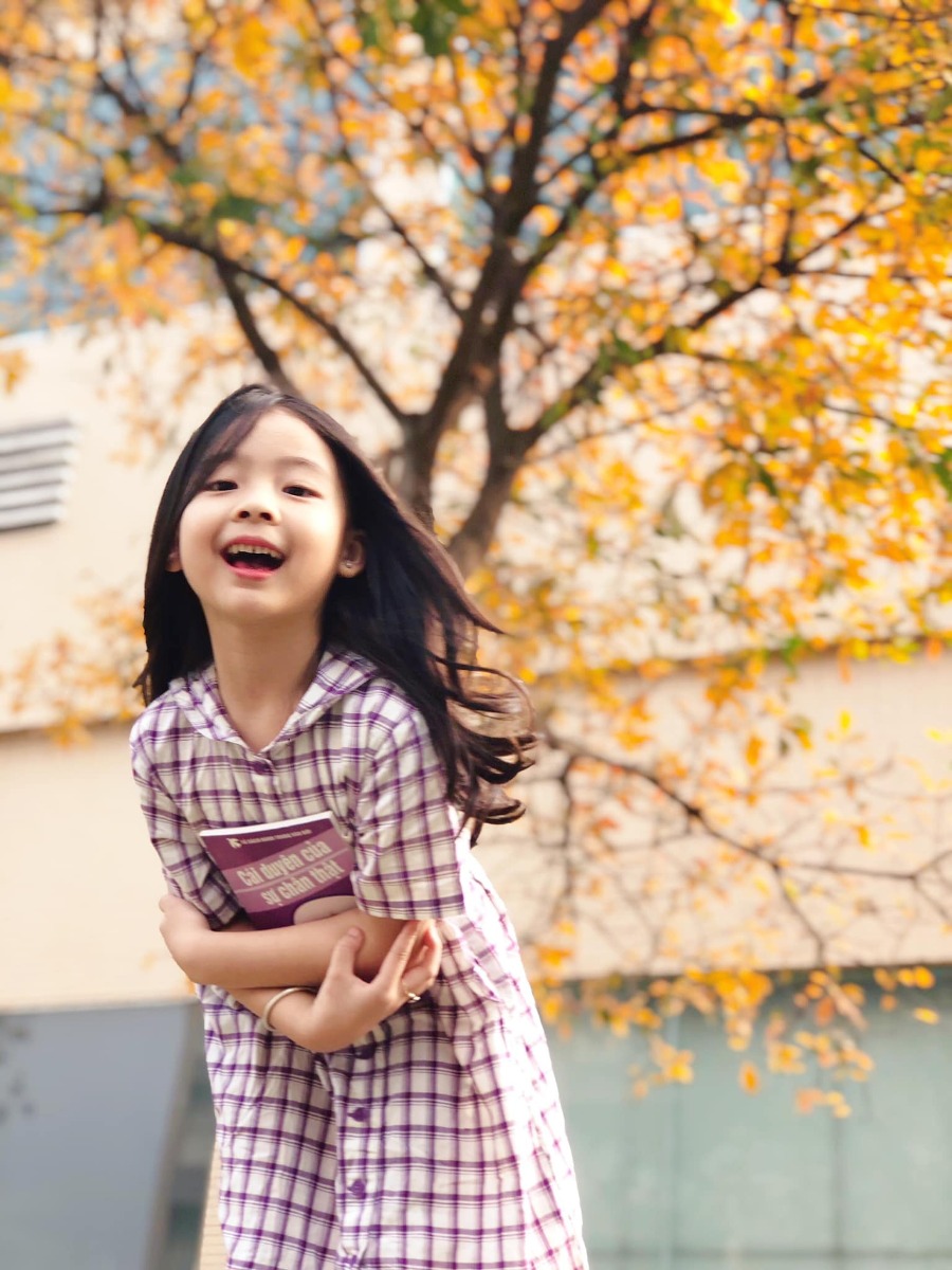 Chào các cô chú, lại là em bé đây ạ. Bữa nay em bé lên công ty mẹ chơi, gặp cây lộc vừng yêu quá nên làm ngay bộ ảnh Hàn Quốc giữa lòng thị trấn nhỏ ạ.
Điện thoại mẹ em bé không hịn lắm nên ảnh hơi kém chất lượng ạ.
Xin phép trình bày quy trình chụp ảnh cho mẫu nhí ạ:
Bước 1: Chọn trang phục và phụ kiện hợp tone màu với cảnh (như bộ này là mẫu mặc sẵn vậy lên công ty mẹ cháu nên cũng không có chuẩn bị trước, nhưng mẹ cháu nhanh mắt nhanh tay kiếm ngay quyển sách tim tím hoa sim mang ra cho đồng bộ).
Bước 2: Ngon ngọt dùng lời động viên, tạo tâm lý thoải mái cho mẫu (có thể tỏ ra đau khổ khi mẫu không hợp tác, tuyệt đối không doạ dẫm). Trêu mẫu, nói chuyện với mẫu tưng bừng lên để bắt khoảnh khắc tự nhiên.
Bước 3: Photographer nằm ngửa ra (dạ, mẹ cháu không nói đùa, chính xác là nằm ngửa ra bãi cỏ chụp từ dưới lên đó ạ vì cái tán cây nó cao lắm).
Bước 4: Mở điện thoại chế độ chân dung, căn cho máy nhận diện và khoá chủ thể (có chữ “ánh sáng tự nhiên “ màu vàng hiện ra là ok) rồi chụp lấy chụp để.
Bước 5: Tải app Meitu, vào phần chỉnh sửa kéo độ sáng, màu sắc lên một xíu, vào filter chọn màu theo tổ tiên mách bảo, không có công thức cố định nào cả, vừa mắt là được thôi. Lưu ý là có thể chồng 1,2,3 filter cho đạt màu ưng ý, có thể crop bớt hoặc xoay cho ảnh cân đối, sau đó vào chỉnh sửa kéo phần “chi tiết” lên (để tăng độ nét).