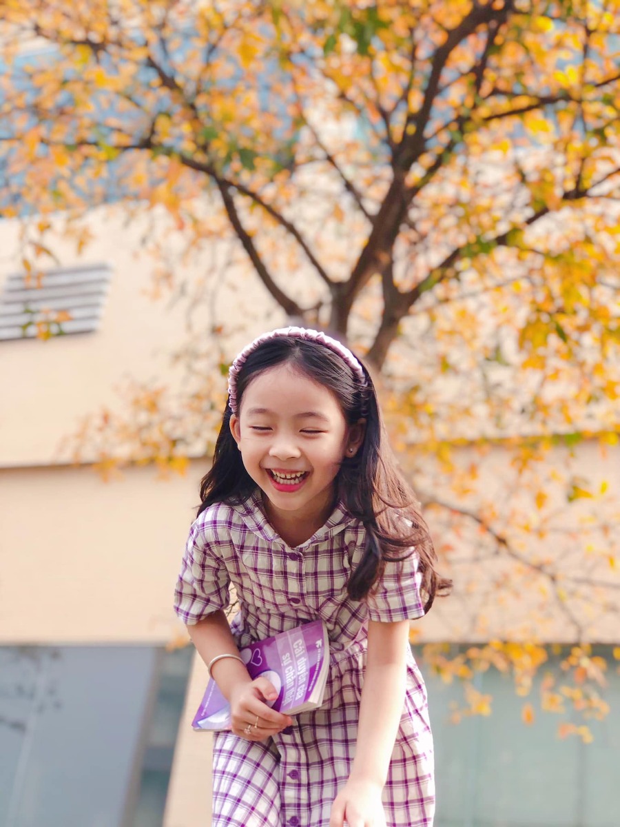 Chào các cô chú, lại là em bé đây ạ. Bữa nay em bé lên công ty mẹ chơi, gặp cây lộc vừng yêu quá nên làm ngay bộ ảnh Hàn Quốc giữa lòng thị trấn nhỏ ạ.
Điện thoại mẹ em bé không hịn lắm nên ảnh hơi kém chất lượng ạ.
Xin phép trình bày quy trình chụp ảnh cho mẫu nhí ạ:
Bước 1: Chọn trang phục và phụ kiện hợp tone màu với cảnh (như bộ này là mẫu mặc sẵn vậy lên công ty mẹ cháu nên cũng không có chuẩn bị trước, nhưng mẹ cháu nhanh mắt nhanh tay kiếm ngay quyển sách tim tím hoa sim mang ra cho đồng bộ).
Bước 2: Ngon ngọt dùng lời động viên, tạo tâm lý thoải mái cho mẫu (có thể tỏ ra đau khổ khi mẫu không hợp tác, tuyệt đối không doạ dẫm). Trêu mẫu, nói chuyện với mẫu tưng bừng lên để bắt khoảnh khắc tự nhiên.
Bước 3: Photographer nằm ngửa ra (dạ, mẹ cháu không nói đùa, chính xác là nằm ngửa ra bãi cỏ chụp từ dưới lên đó ạ vì cái tán cây nó cao lắm).
Bước 4: Mở điện thoại chế độ chân dung, căn cho máy nhận diện và khoá chủ thể (có chữ “ánh sáng tự nhiên “ màu vàng hiện ra là ok) rồi chụp lấy chụp để.
Bước 5: Tải app Meitu, vào phần chỉnh sửa kéo độ sáng, màu sắc lên một xíu, vào filter chọn màu theo tổ tiên mách bảo, không có công thức cố định nào cả, vừa mắt là được thôi. Lưu ý là có thể chồng 1,2,3 filter cho đạt màu ưng ý, có thể crop bớt hoặc xoay cho ảnh cân đối, sau đó vào chỉnh sửa kéo phần “chi tiết” lên (để tăng độ nét).